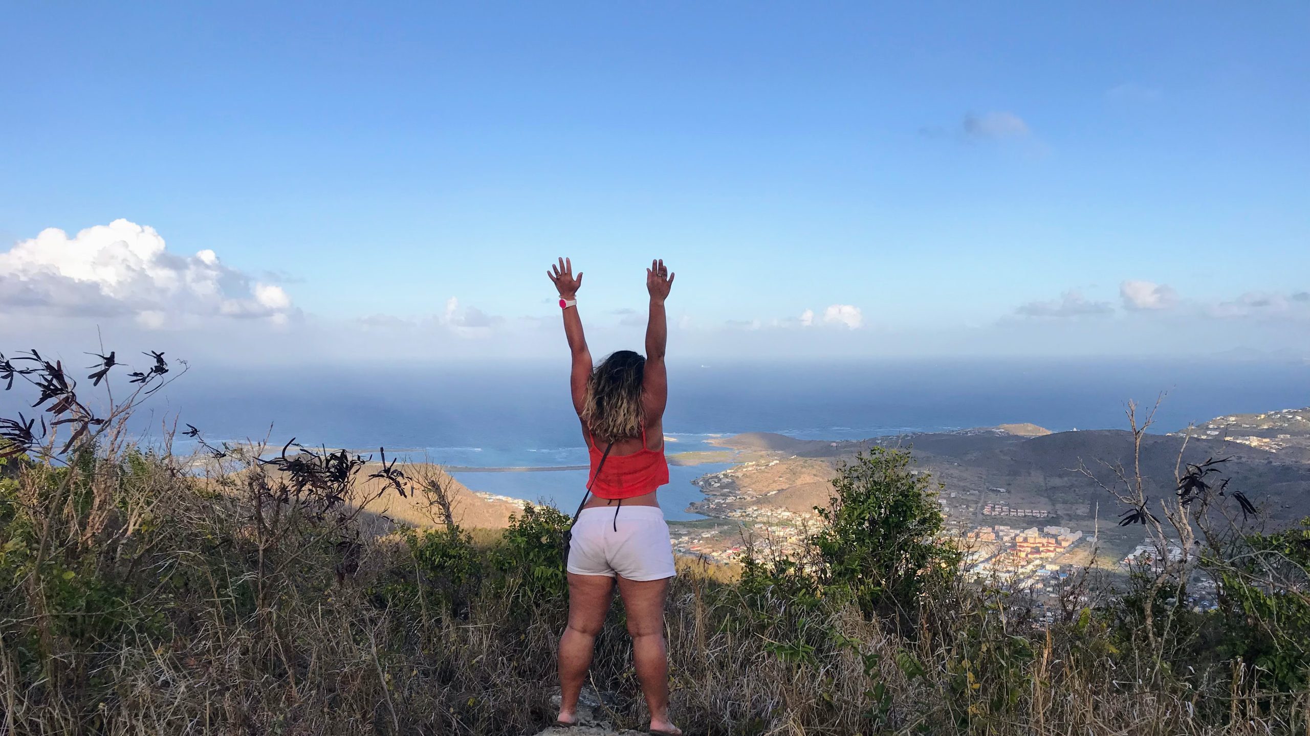 Women celebrating her achievement. She hiked the mountain and overlooking a beautiful bay. Sint Maarten, Netherlands Antillies.
